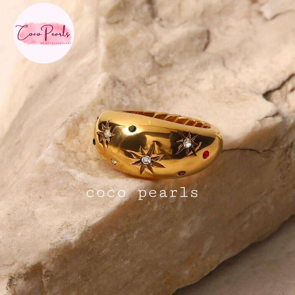 Coco pearls stainless Steel gold ring with star and diamond motifs, displayed on a textured beige stone surface.