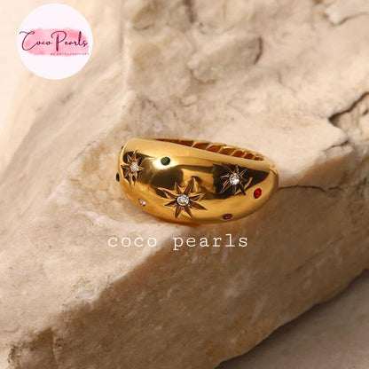 Coco pearls stainless Steel gold ring with star and diamond motifs, displayed on a textured beige stone surface.
