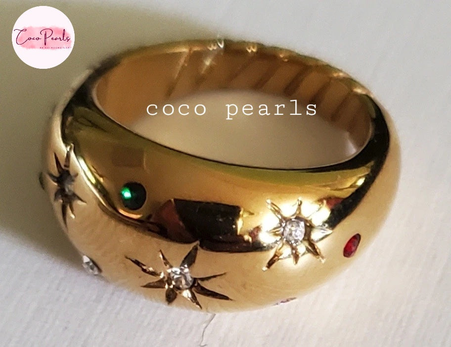 Coco pearls stainless Steel anti tarnish gold ring with starburst motifs set with small diamonds and a green and red gemstone, shown on a light background
