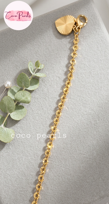 Coco pearls stainless Steel anti tarnish gold chain accessory with a textured sunburst heart charm and lobster clasp, displayed on a gray velvet surface 
