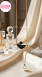 Coco pearls stainless Steel anti tarnish gold-tone necklace with a black crystal swan pendant and a dangling white pearl, displayed on draped cream fabric