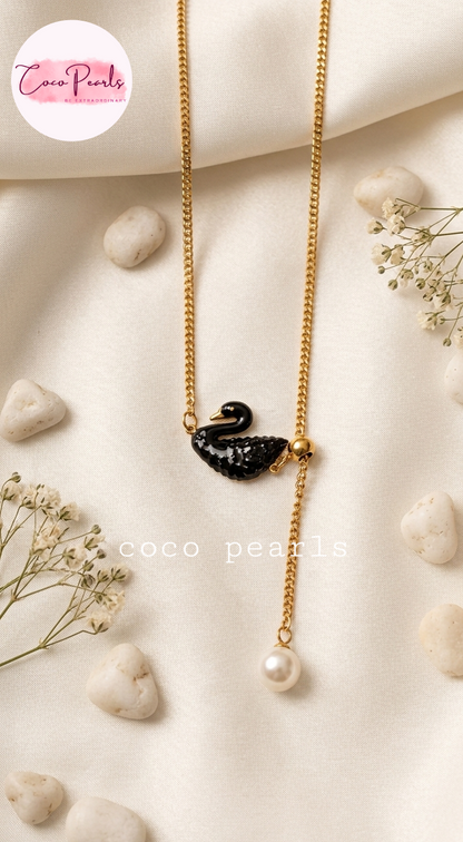 Coco pearls stainless Steel anti tarnish gold-tone dangle necklace with a black swan pendant and a dangling pearl, styled on a cream fabric background