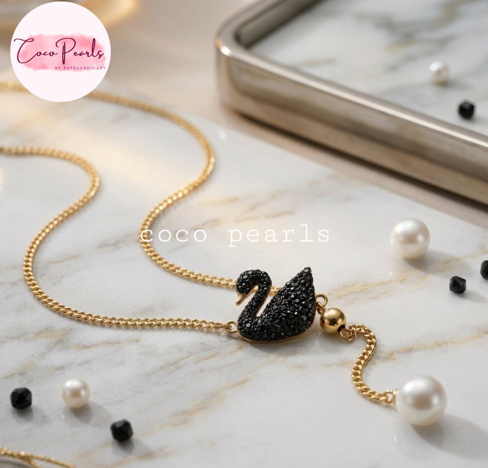 Coco pearls stainless Steel anti tarnish gold chain necklace with a black crystal-embellished swan pendant, styled on a white marble surface 
