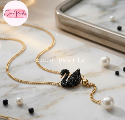 Coco pearls stainless Steel anti tarnish gold chain necklace with a black crystal-embellished swan pendant, styled on a white marble surface 