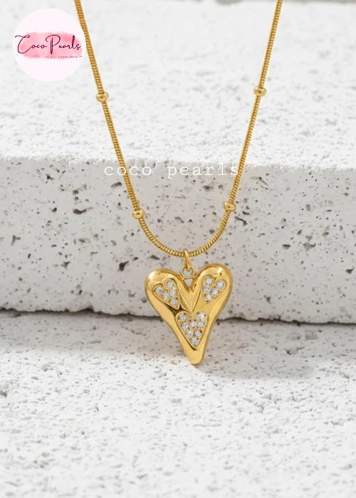 Coco pearls stainless Steel anti tarnish gold heart-shaped pendant necklace with small clear stones set along the edges, hanging from a delicate gold chain against a light textured stone background.