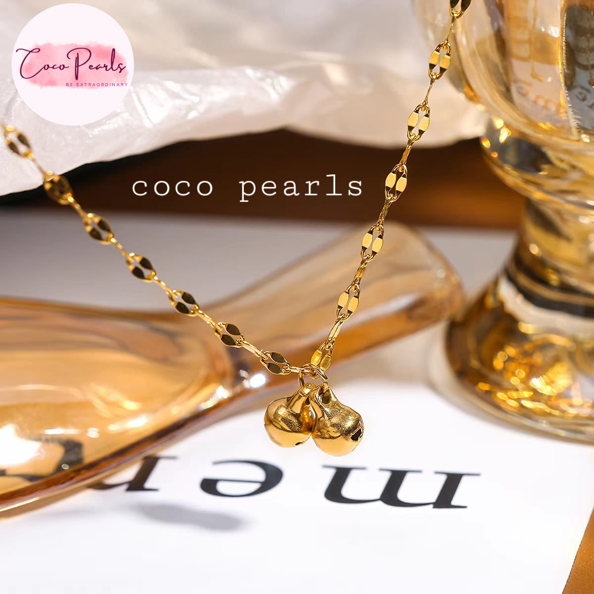 Coco pearls stainless Steel anti tarnish gold-tone necklace with two small hanging bells, styled on a glossy surface 