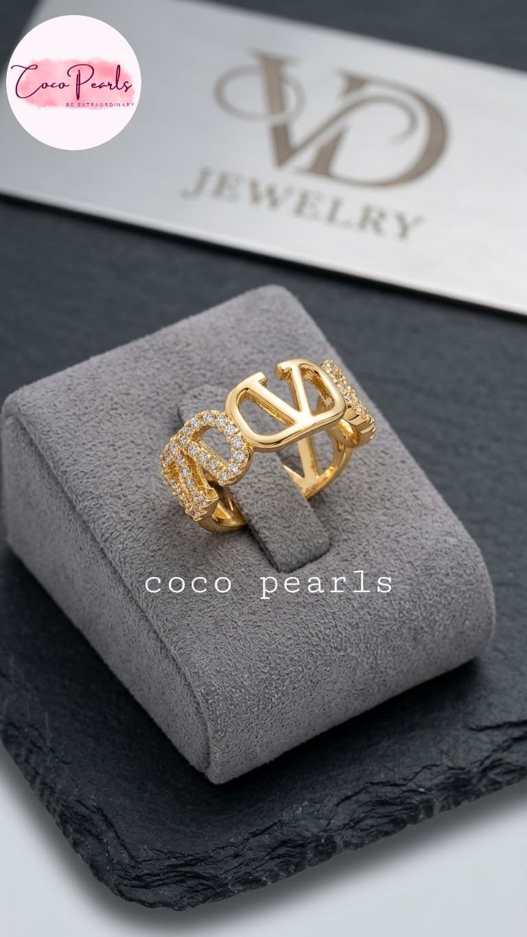Coco pearls stainless Steel anti tarnish gold ring with a large interlocking 'CO' design and textured side details, displayed on a gray velvet jewelry box.