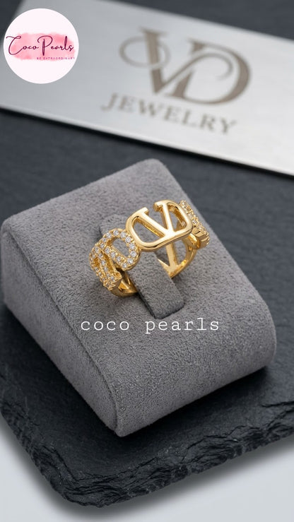 Coco pearls stainless Steel anti tarnish gold ring with a large interlocking 'CO' design and textured side details, displayed on a gray velvet jewelry box.