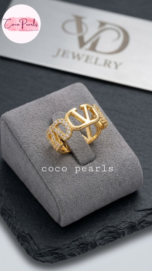 Coco pearls stainless Steel anti tarnish gold ring with a large interlocking 'CO' design and textured side details, displayed on a gray velvet jewelry box.