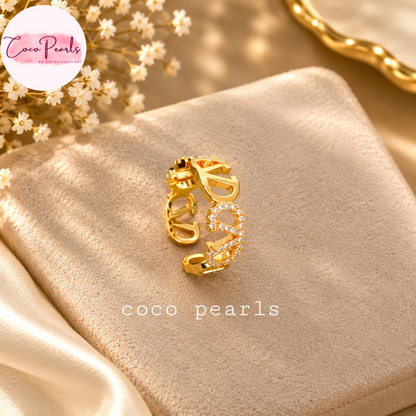 Coco pearls stainless Steel anti tarnish gold open ring earring with the word 'coco' embellished with clear rhinestones, displayed on a beige velvet surface