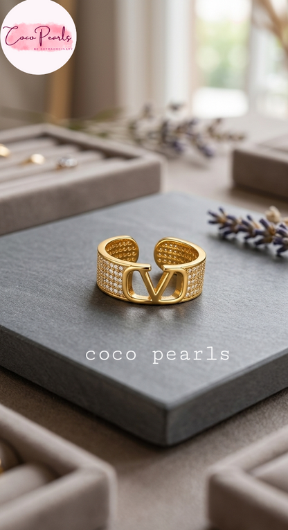 Coco pearls stainless Steel anti tarnish gold-toned open cuff ring with a large interlocking V motif and rows of small clear stones, displayed on a dark gray stone slab 