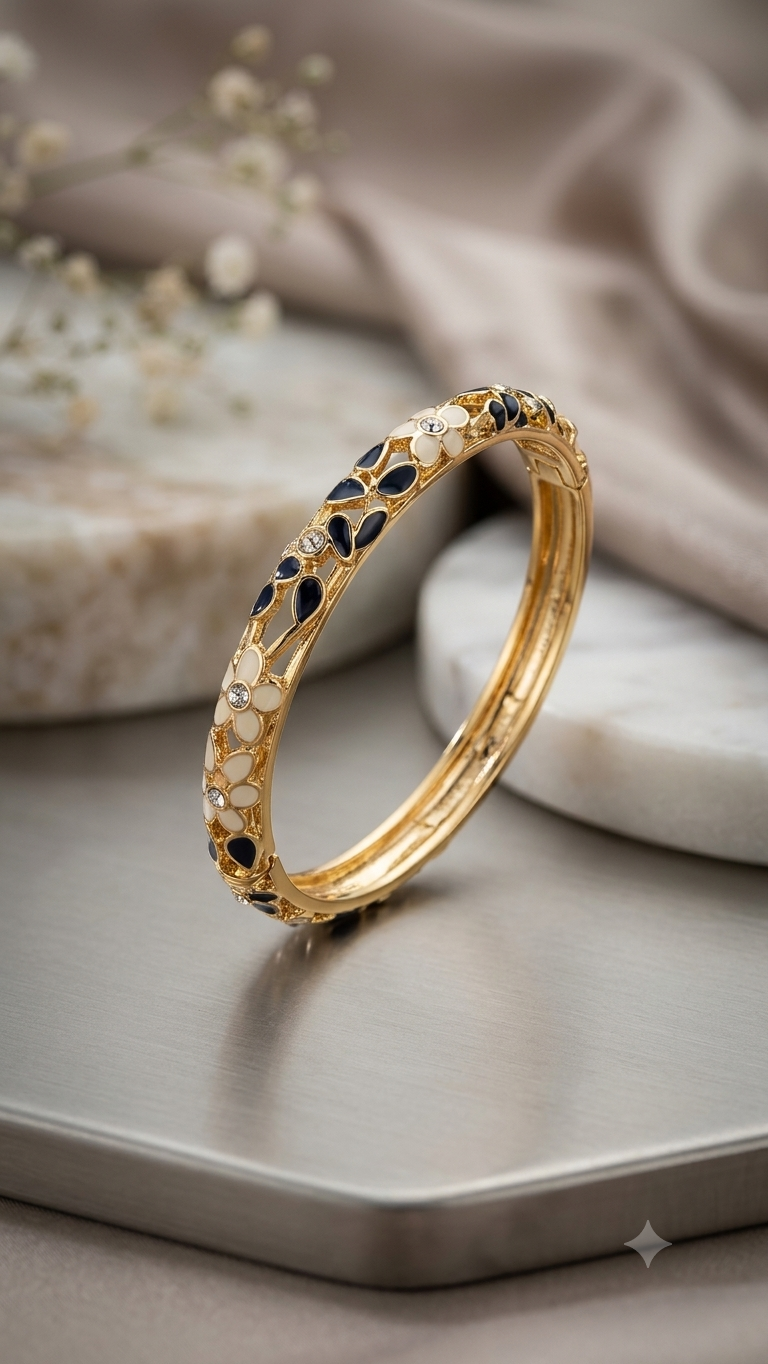  Coco pearls  gold plated bangle bracelet with black and white floral engravings, displayed on a gray tray with a beige fabric background.