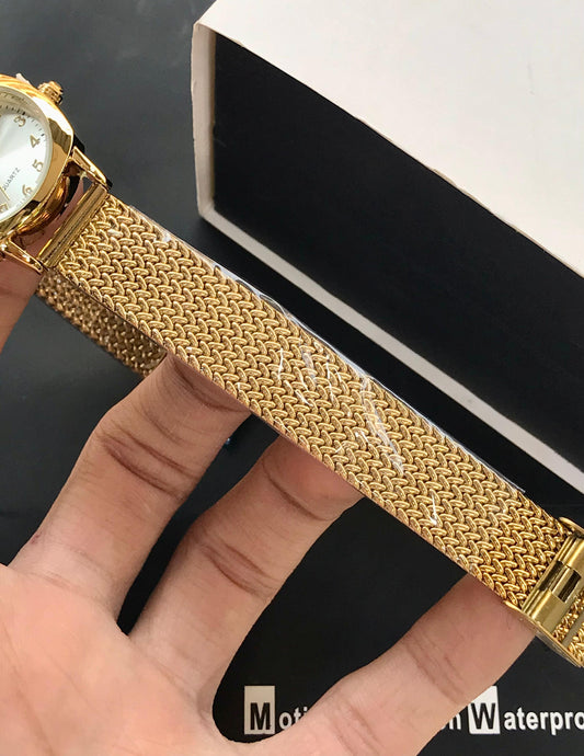 Gold watch with a textured band held by a hand against a black and white background