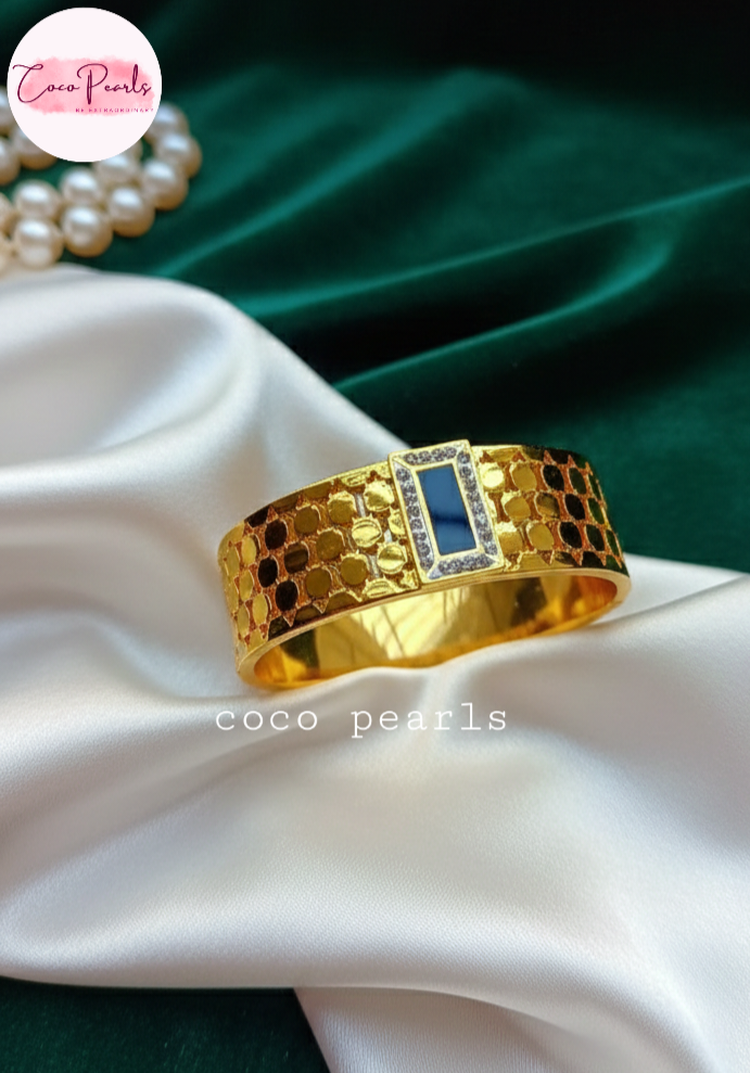 coco pearls stainless steel Gold azure handcuff bangle bracelet with black in center surrounded by gemstones on a white fabric background