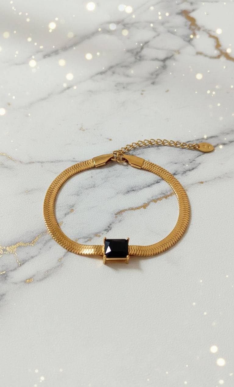 Coco Pearls Stainless Steel Anti Tarnish Gold black accent bracelet with a black gemstone on snake chain on a marble background