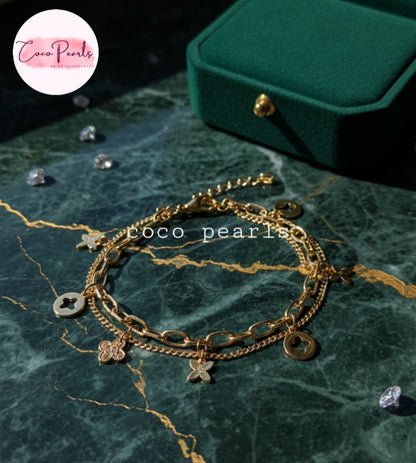 Coco Pearls Stainless steel anti tarnish Gold charm layered bracelets with charms on a green marble surface