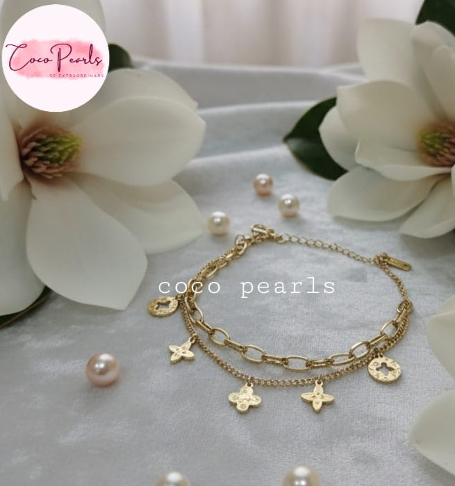 Coco Pearls Stainless steel anti tarnish Gold bracelet with star charms and pearls on a white surface with white flowers in background