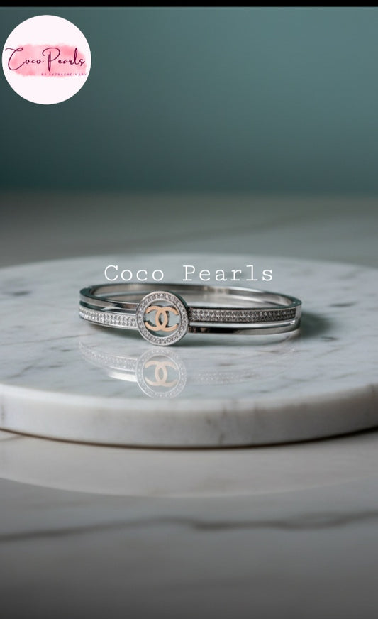 Coco Pearls Stainless Steel Anti Tarnish Silver coco charm handcuff bangle  bracelet with diamond studded Chanel logo on a marble surface