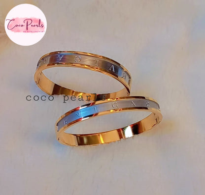 Coco Pearls Stainless Steel Anti Tarnish Two coco glitz gold and silver handcuff bangle bracelets with engraved text on a light background