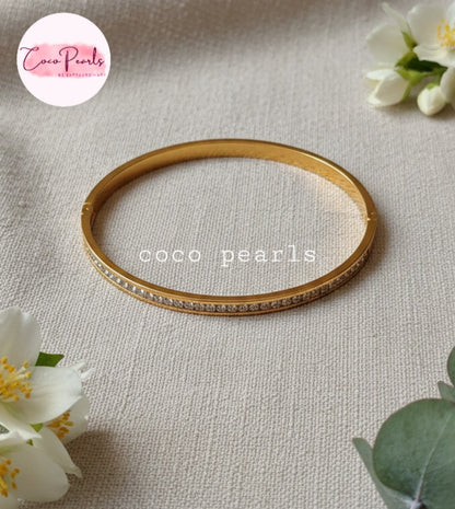 Coco Pearls Stainless Steel Anti tarnish Gold  crystal shine handcuff bracelet with clear stones displayed on a beige background 