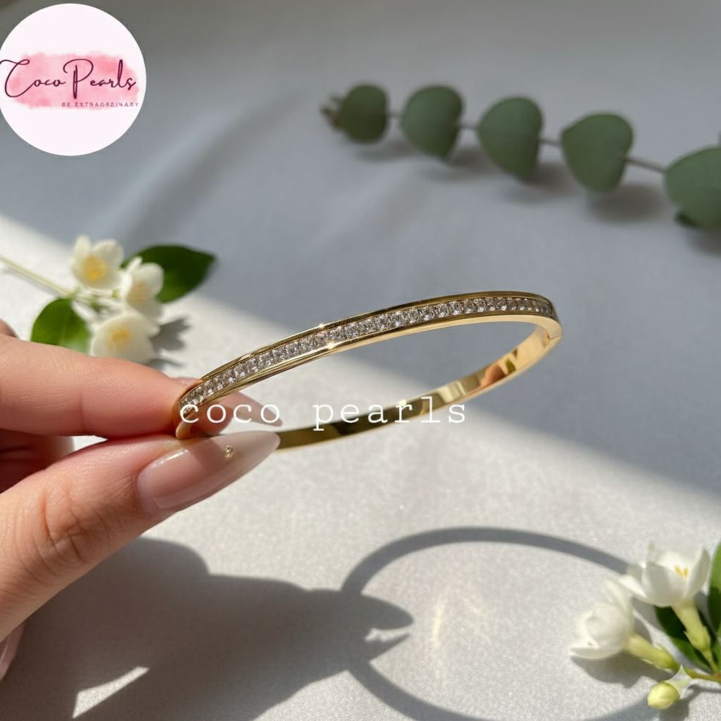Coco Pearls Stainless Steel Anti tarnish gold crystal shine handcuff bracelet with clear stones held by a hand on a light background