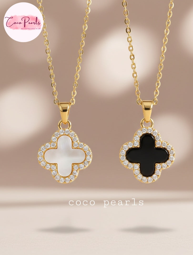 Coco Pearls Stainless Steel Anti Tarnish Two sided diamond studded gold necklaces with clover-shaped pendants one side black one side white on a beige surface.