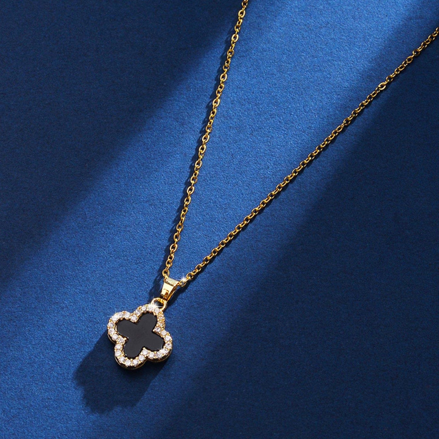 Coco Pearls Stainless Steel Anti Tarnish Two sided diamond studded gold necklaces with clover-shaped pendants one side black one side white on a blue surface.
