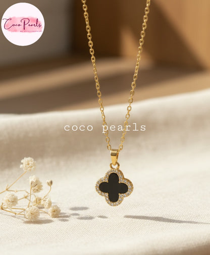 Coco Pearls Stainless Steel Anti Tarnish Two sided diamond studded gold necklaces with clover-shaped pendants one side black one side white on a beige surface.