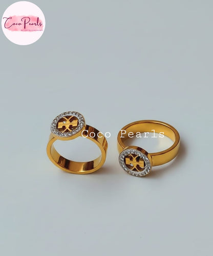 Coco Pearls Stainless Steel Anti Tarnish Two dazzle gold rings with decorative elements. diamond studded circular charm on a light gray background