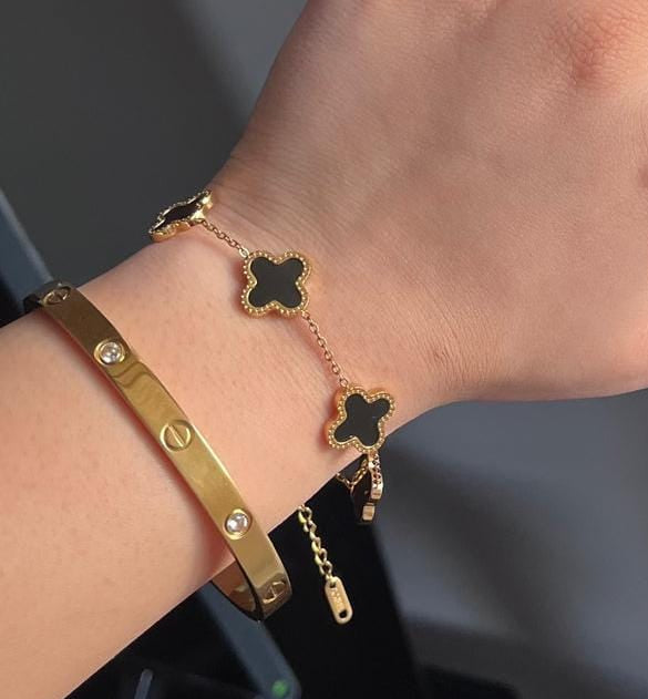 Coco Pearls Stainless Steel Anti Tarnish Gold dazzling grace combo bracelet with black clover charms  and Cartier handcuff on a wrist against a dark background
