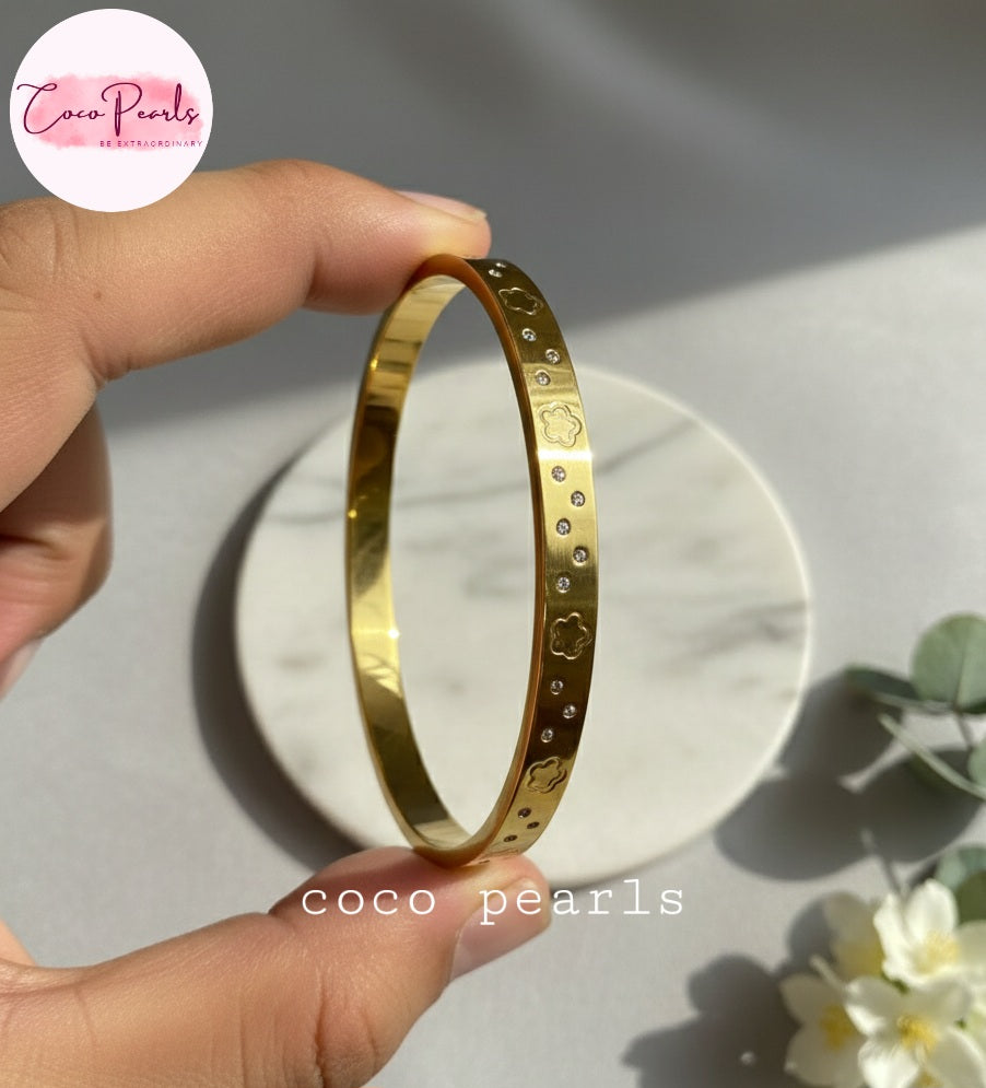 Coco Pearls Stainless Steel Anti tarnish Gold diamond groove handcuff bracelet held by a hand on a marble surface