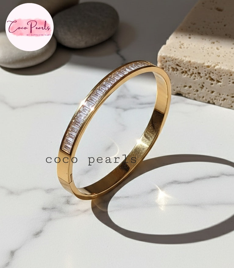 Coco Pearls Stainless Steel Anti Tarnish Gold diamond line handcuff bracelet with clear stones on a marble surface