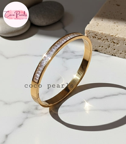 Coco Pearls Stainless Steel Anti Tarnish Gold diamond line handcuff bracelet with clear stones on a marble surface