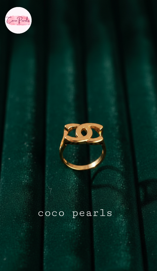coco pearls stainless steel anti tarnish Gold ring with a logo on a green textured background