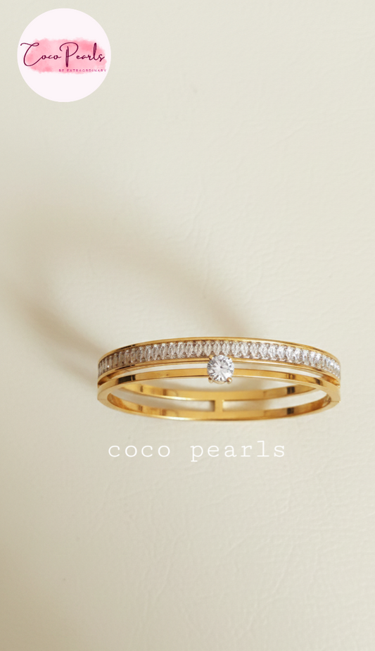 Coco Pearls Stainless Steel Anti tarnish Gold eternal gleam handcuff bangle bracelet with a small gemstone in center and clear stones on a white surface