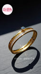 Coco Pearls Stainless Steel Anti tarnish Gold eternal gleam handcuff bangle bracelet with a small gemstone in center and clear stones on a white surface