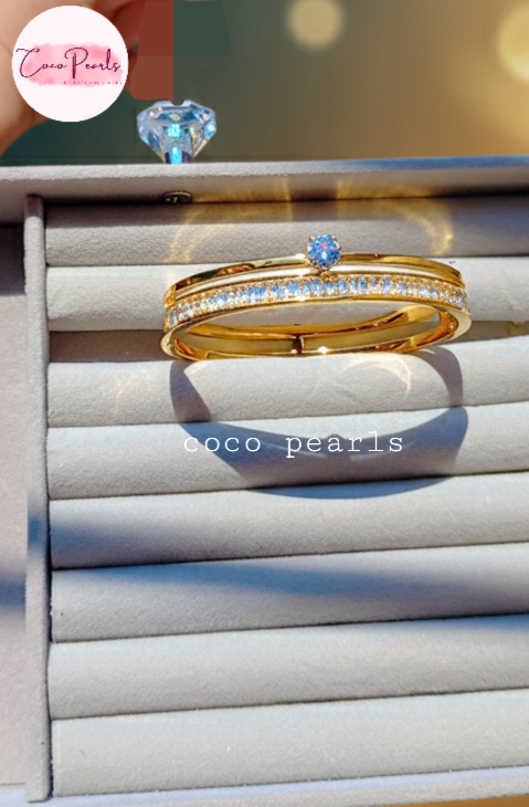 Coco Pearls Stainless Steel Anti tarnish Gold eternal gleam handcuff bangle bracelet with a small gemstone in center and clear stones on a white surface