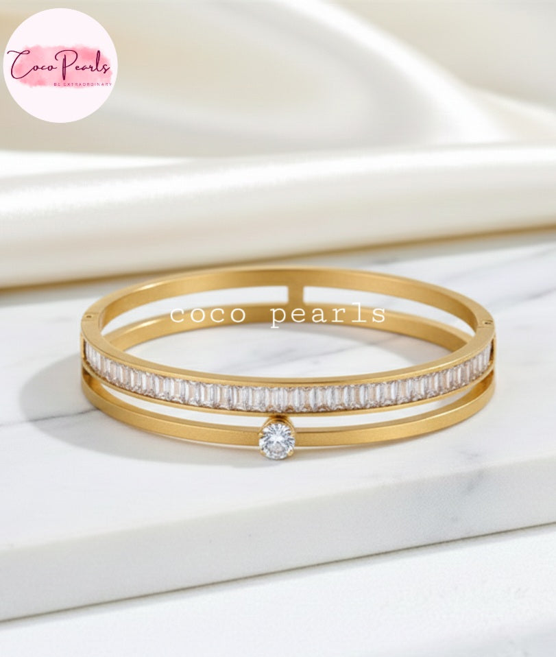 Coco Pearls Stainless Steel Anti tarnish Gold eternal gleam handcuff bangle bracelet with a small gemstone in center and clear stones on a white surface