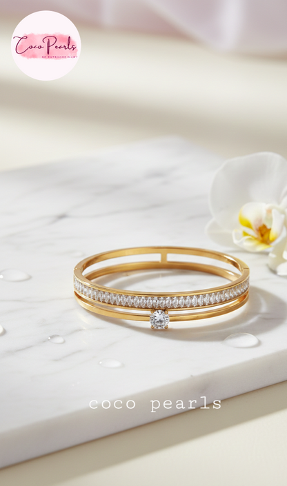 Coco Pearls Stainless Steel Anti tarnish Gold eternal gleam handcuff bangle bracelet with a small gemstone in center and clear stones on a white surface