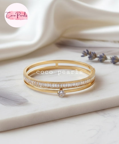 Coco Pearls Stainless Steel Anti tarnish Gold eternal gleam handcuff bangle bracelet with a small gemstone in center and zircon studded on a white surface