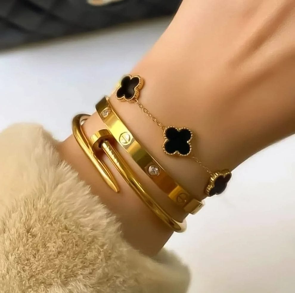 Coco Pearls Stainless Steel Anti Tarnish Golden grace bracelet combo with black clover designs bracelet, cartier handcuff and nail handcuff on a wrist against a neutral background
