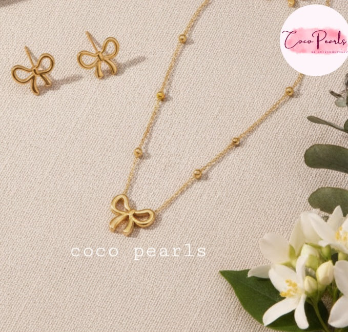 Coco Pearls Stainless Steel Anti tarnish Gold bow-shaped necklace and earrings on a beige fabric background 