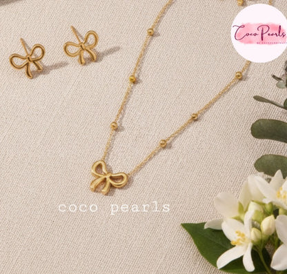 Coco Pearls Stainless Steel Anti tarnish Gold bow-shaped necklace and earrings on a beige fabric background 