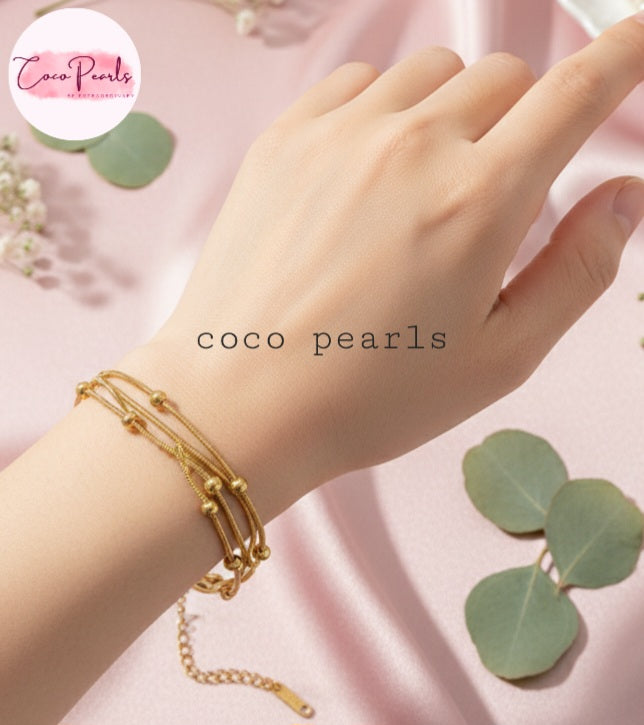 Coco Pearls Stainless steel Anti Tarnish Golden harmony bracelet with three layer ball chain on a wrist with  pink background with green leaves.