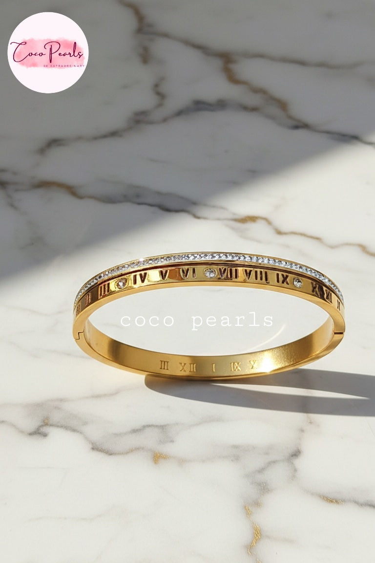 coco pearls stainless steel anti tarnish golden hour handcuff with roman number and diamond studded line displayed on marble surface