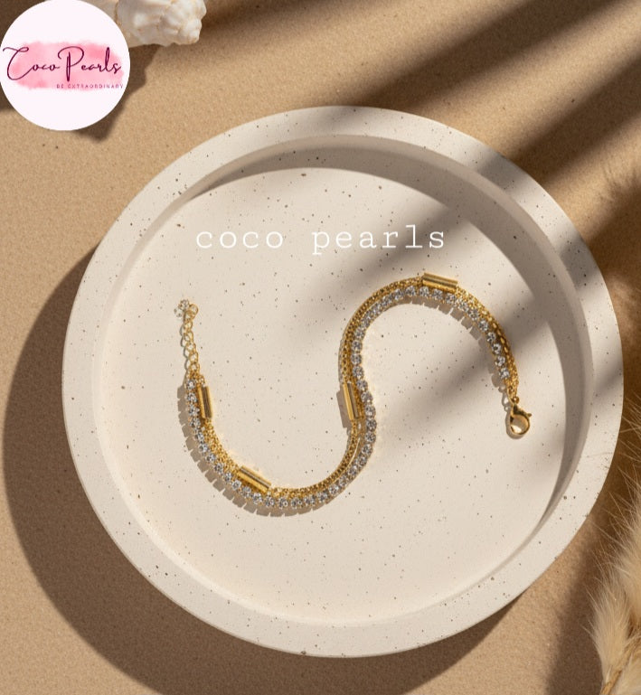Coco Pearls Stainless steel Anti Tarnish Golden stream link bracelet with double layer chain. a diamond studded line and golden chain displayed on a  beige plate