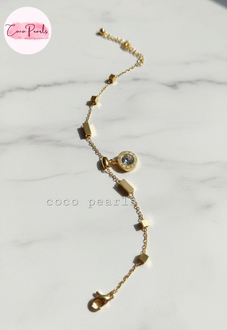 Coco Pearls Stainless steel anti tarnish Gold geometry bracelet with gemstone hanging displayed on a marble background,