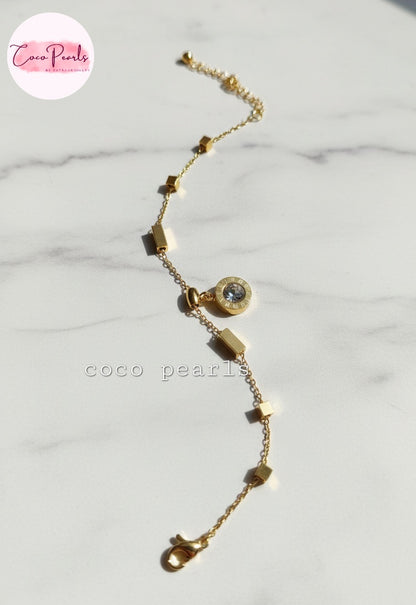Coco Pearls Stainless steel anti tarnish Gold geometry bracelet with gemstone hanging displayed on a marble background,