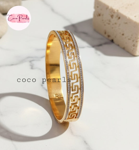 Coco Pearls Stainless Steel Anti Tarnish Gold greco glam bangle bracelet with intricate design on a marble surface