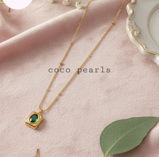 Coco Pearls Stainless Steel Anti Tarnish Gold green gem necklace with a green pendant on a pink fabric background